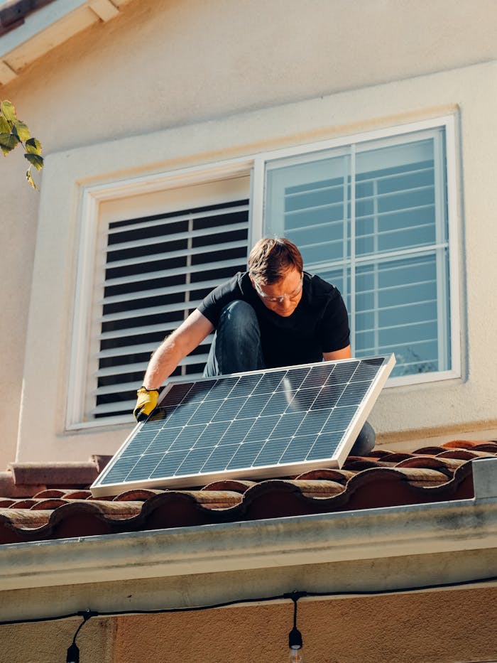 creative-03 A worker installing a solar panel on a residential rooftop under bright sunlight.